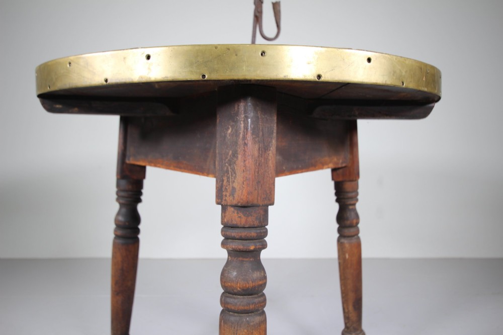 An early nineteenth-century wooden cricket table featuring a circular plank top with a brass-bound rim supported on three turned legs. View III