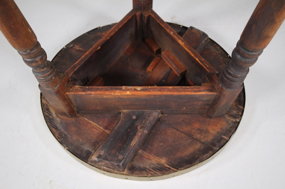 An early nineteenth-century wooden cricket table featuring a circular plank top with a brass-bound rim supported on three turned legs. View IV