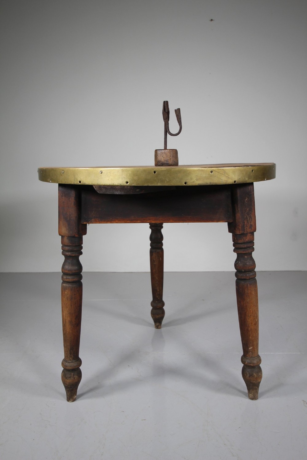 An early nineteenth-century wooden cricket table featuring a circular plank top with a brass-bound rim supported on three turned legs. View V