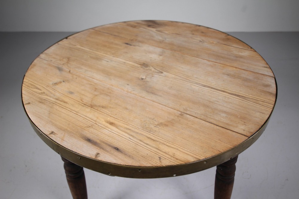 An early nineteenth-century wooden cricket table featuring a circular plank top with a brass-bound rim supported on three turned legs. View VI