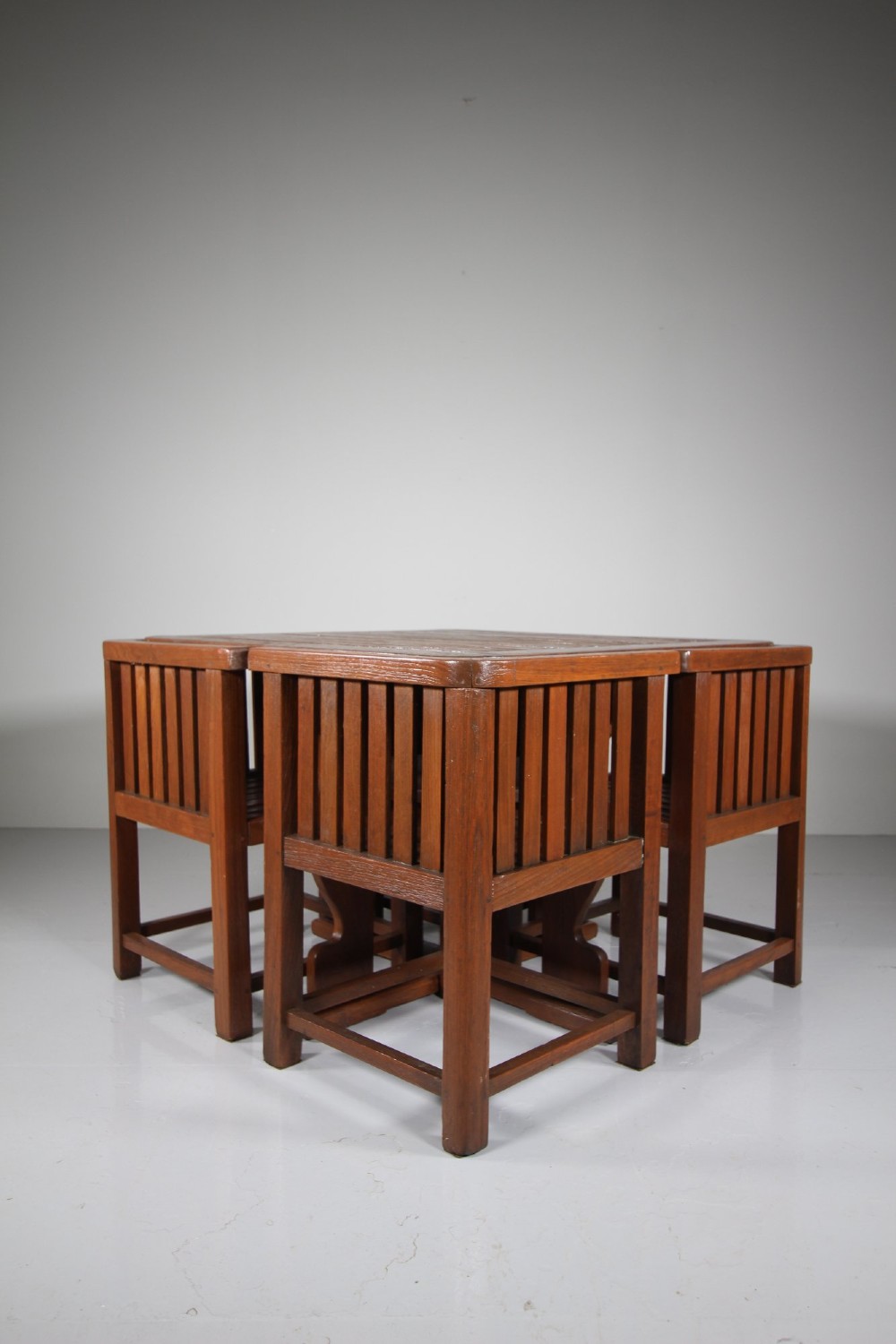 A 1920s slatted teak garden dining set featuring a square table and four corner chairs that tuck flush under the tabletop. View V