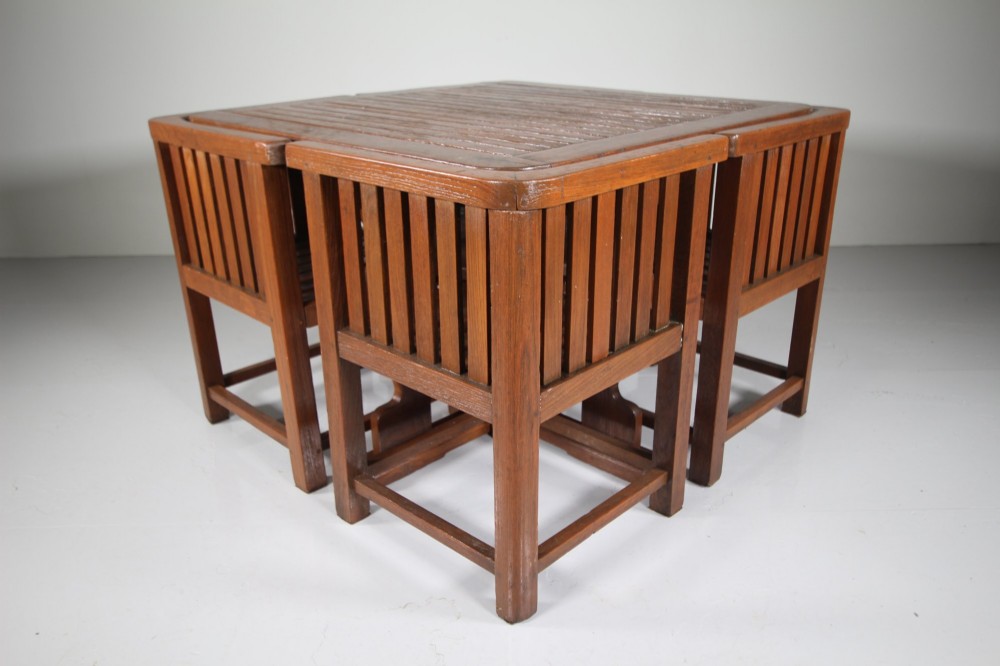 A 1920s slatted teak garden dining set featuring a square table and four corner chairs that tuck flush under the tabletop. View VI