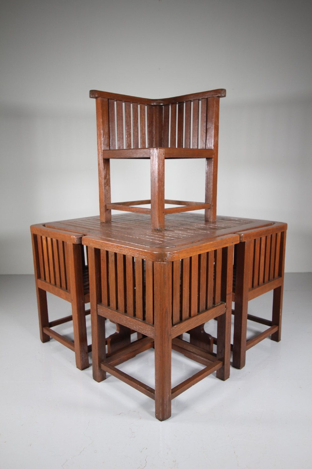 A 1920s slatted teak garden dining set featuring a square table and four corner chairs that tuck flush under the tabletop. View VII