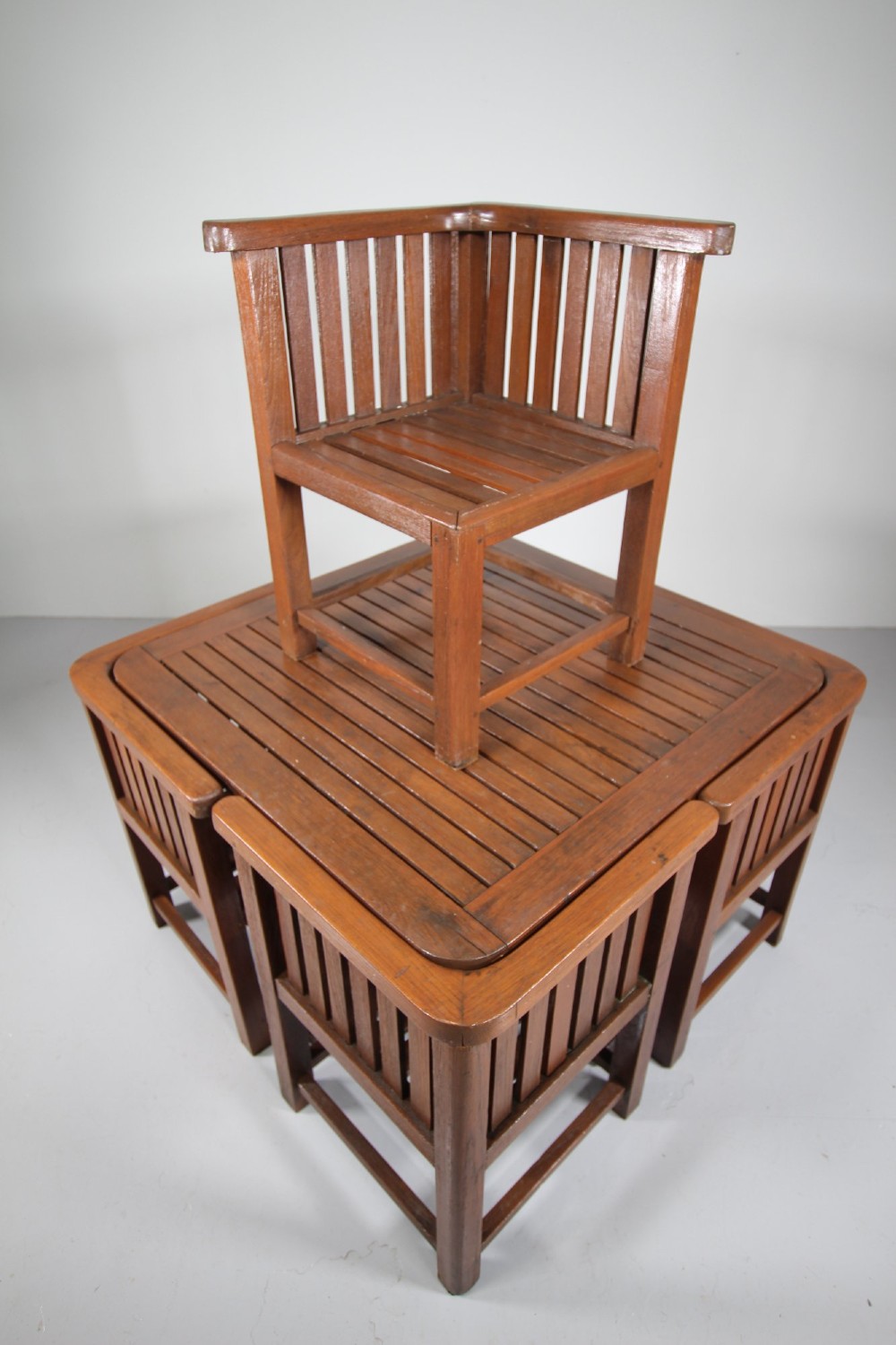 A 1920s slatted teak garden dining set featuring a square table and four corner chairs that tuck flush under the tabletop. View VIII
