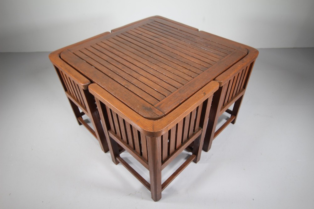 A 1920s slatted teak garden dining set featuring a square table and four corner chairs that tuck flush under the tabletop. View IX