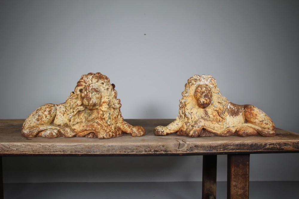 A pair of 19th-century cast iron recumbent lion boot scrapers featuring weathered cream paint and visible rust patination. View V