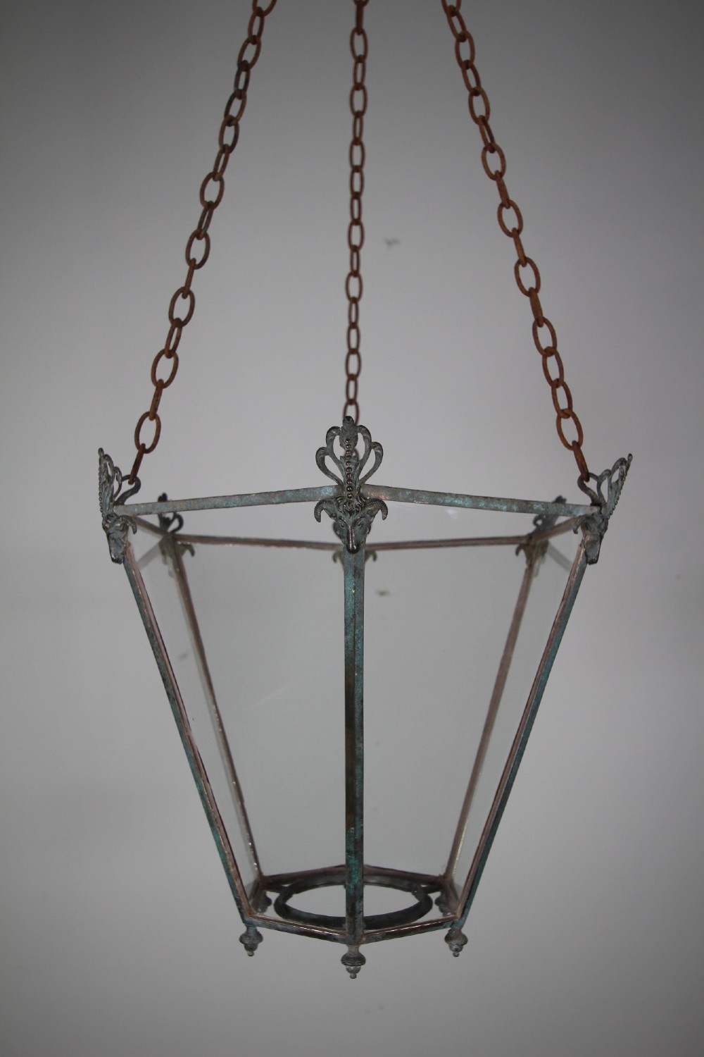 An early nineteenth-century tapered hexagonal bronze hanging lantern featuring cast ram head motifs, clear glass panels, and suspension chains.