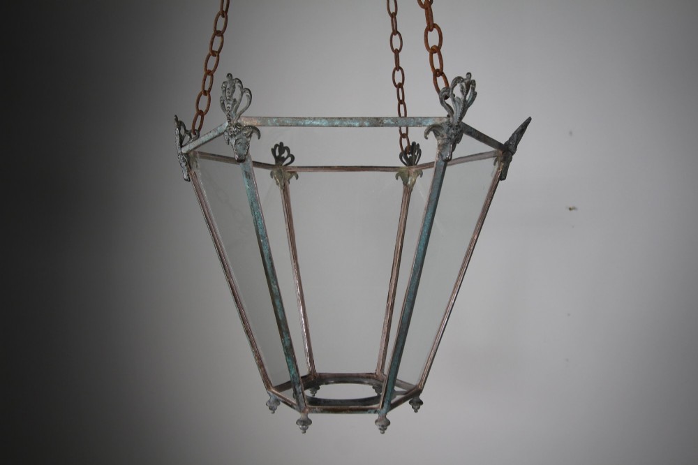An early nineteenth-century tapered hexagonal bronze hanging lantern featuring cast ram head motifs, clear glass panels, and suspension chains. View II