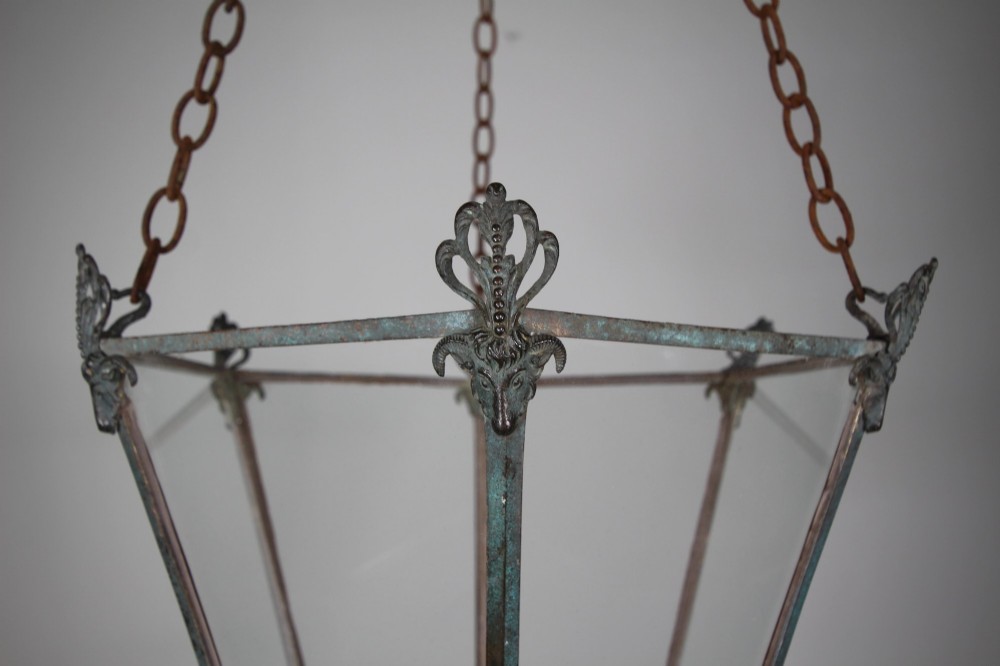 An early nineteenth-century tapered hexagonal bronze hanging lantern featuring cast ram head motifs, clear glass panels, and suspension chains. View III