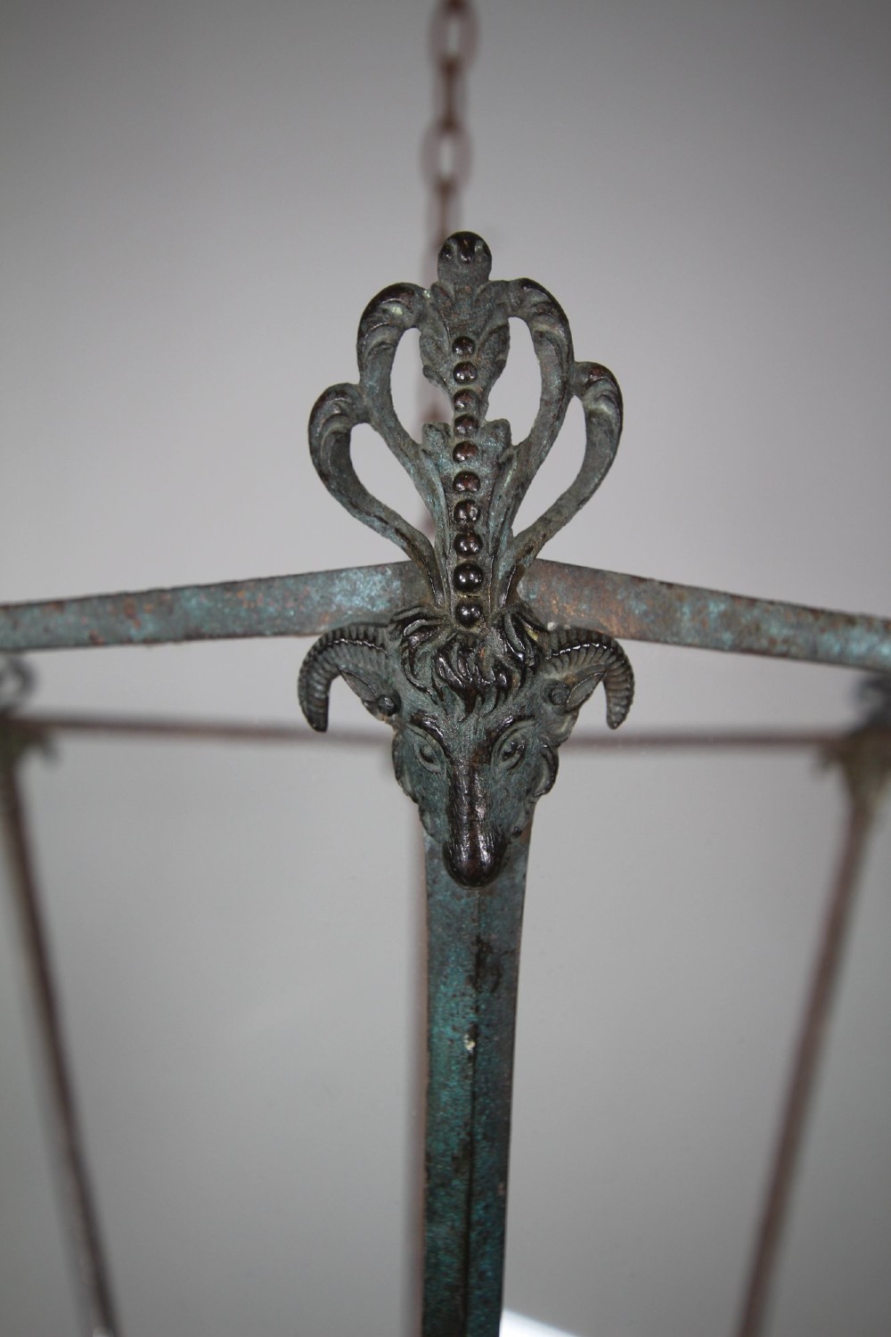 An early nineteenth-century tapered hexagonal bronze hanging lantern featuring cast ram head motifs, clear glass panels, and suspension chains. View IV