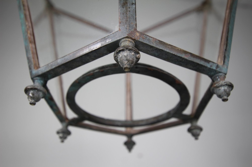 An early nineteenth-century tapered hexagonal bronze hanging lantern featuring cast ram head motifs, clear glass panels, and suspension chains. View V