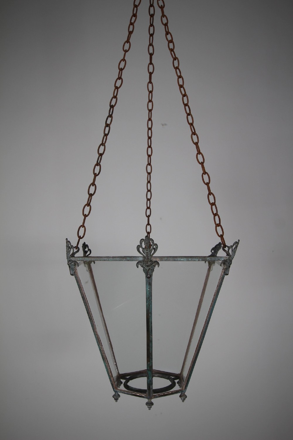 An early nineteenth-century tapered hexagonal bronze hanging lantern featuring cast ram head motifs, clear glass panels, and suspension chains. View VI