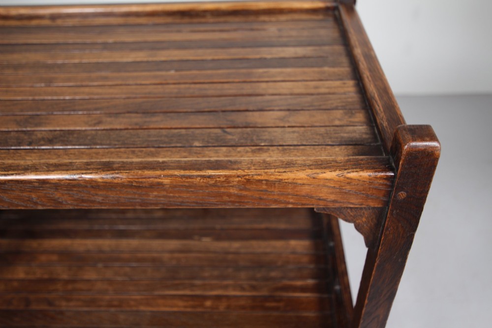 A dark oak three-tiered Edwardian trolley featuring slatted shelf galleries and castor wheels. View V