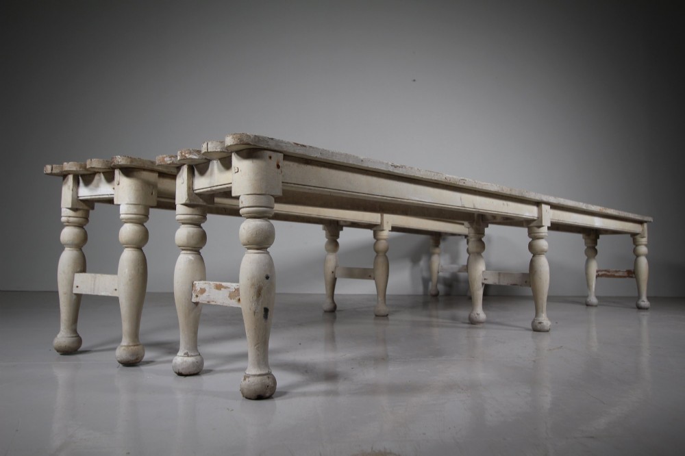 A pair of long 19th-century painted pine greenhouse benches featuring slatted tops and turned legs with lower stretchers.