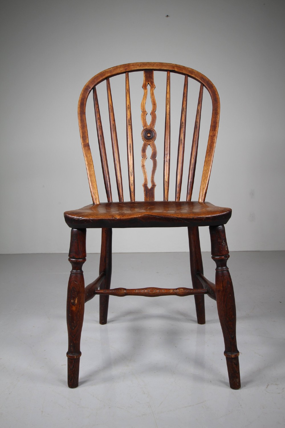 An early 19th-century hoop back Windsor chair crafted from dark elm, featuring a pierced central splat, turned legs, and a contoured saddle seat. View II