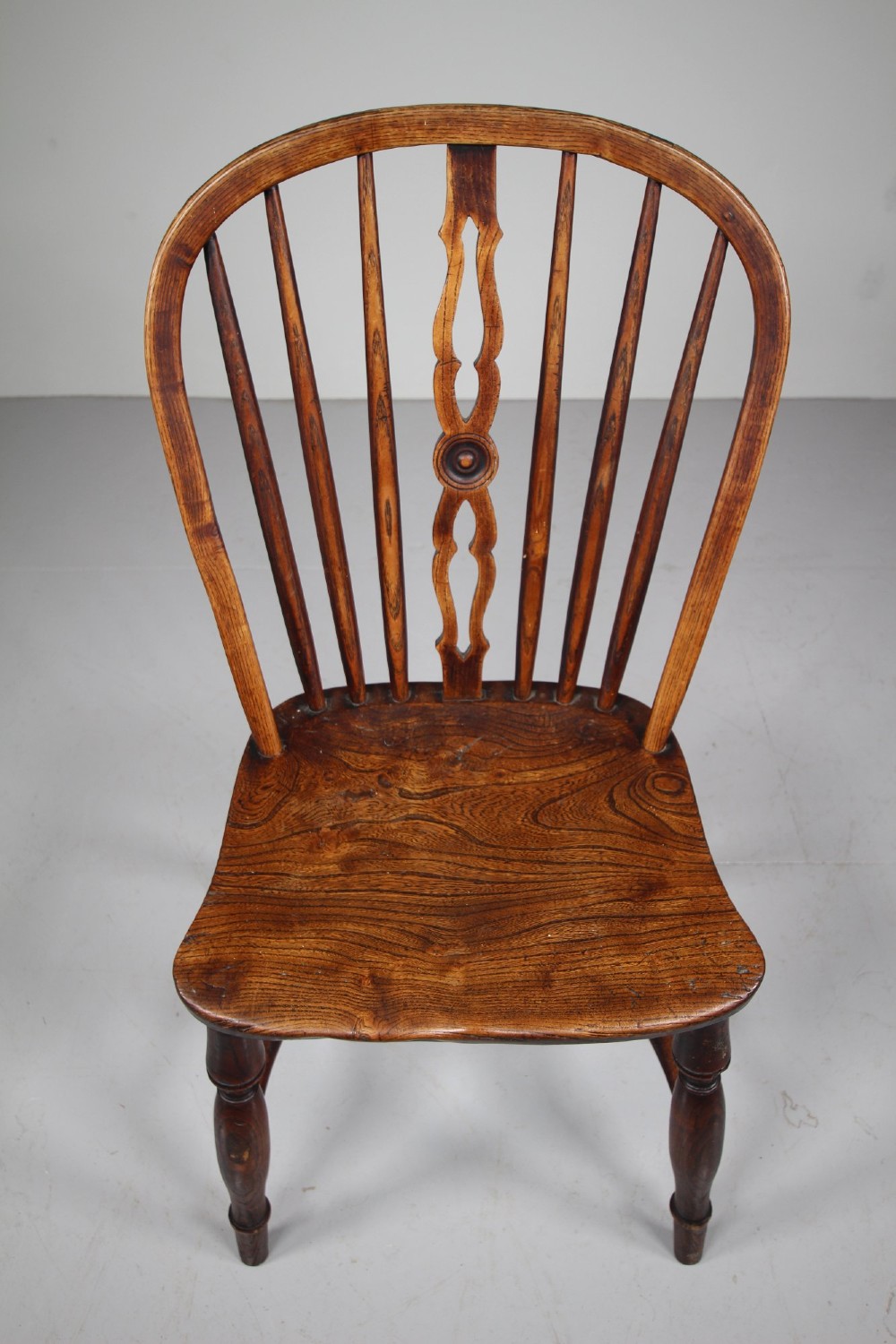 An early 19th-century hoop back Windsor chair crafted from dark elm, featuring a pierced central splat, turned legs, and a contoured saddle seat. View III