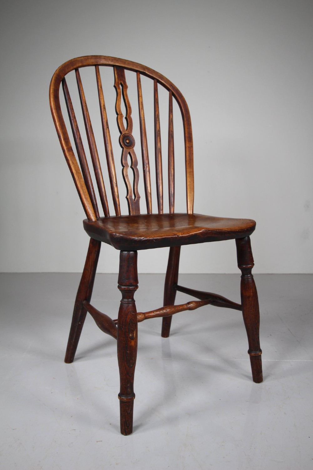 An early 19th-century hoop back Windsor chair crafted from dark elm, featuring a pierced central splat, turned legs, and a contoured saddle seat. View V