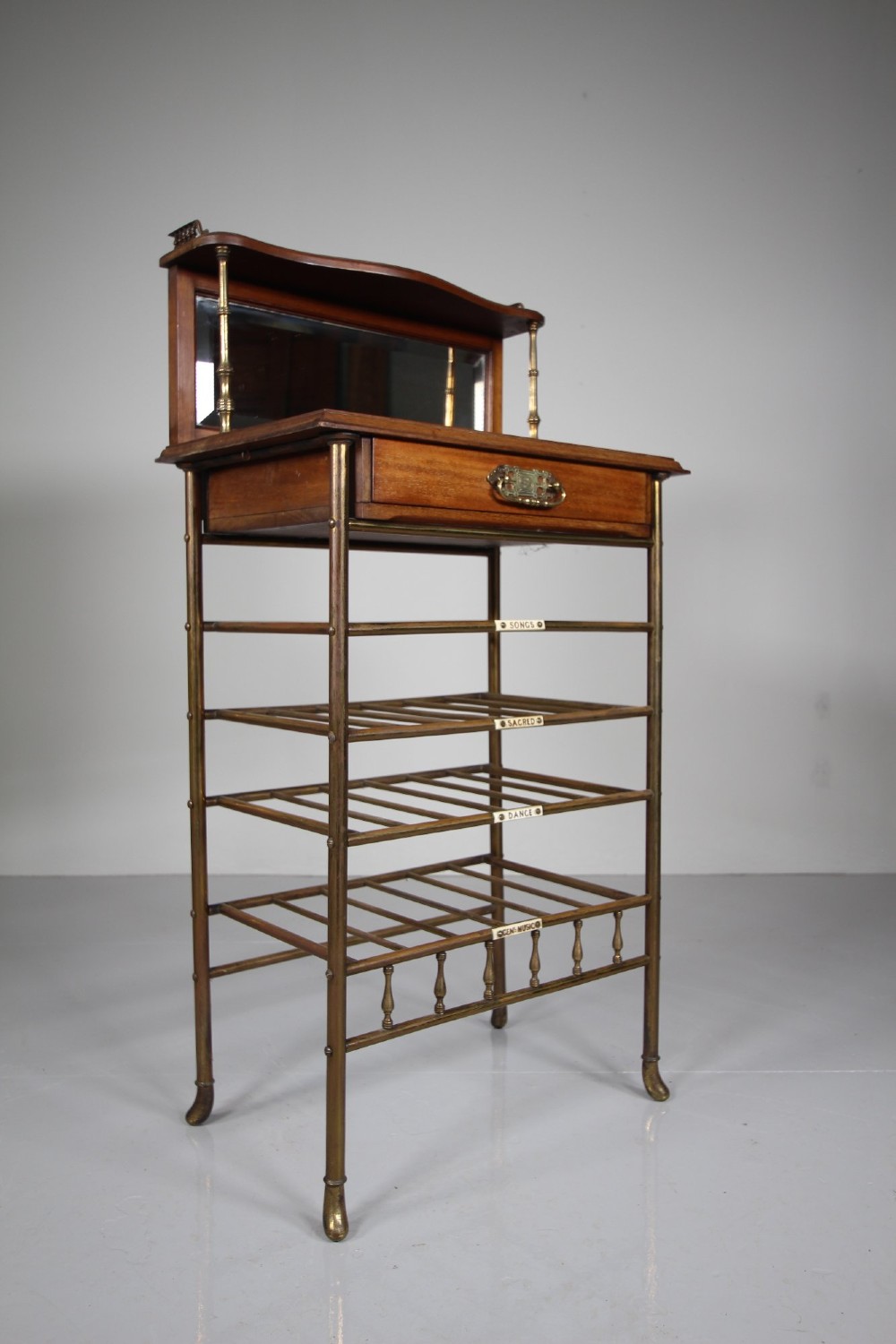 A 19th-century English Victorian brass and mahogany sheet music stand featuring open slatted shelves with ceramic labels, a top drawer, and a mirrored upper gallery. View III