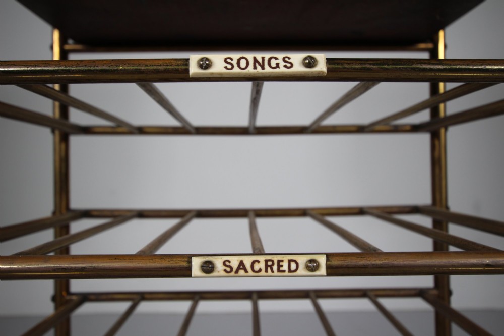 A 19th-century English Victorian brass and mahogany sheet music stand featuring open slatted shelves with ceramic labels, a top drawer, and a mirrored upper gallery. View V