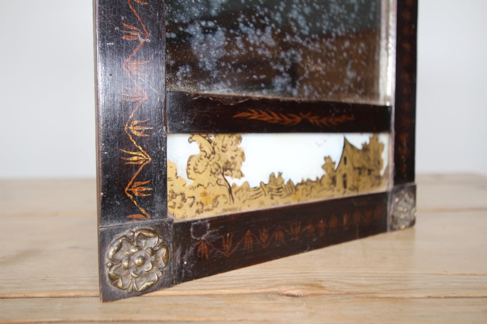 An early 19th-century rectangular wall mirror featuring a dark painted wooden frame with stencilled foliate borders and two reverse-painted glass panels displaying rural landscape scenes. View II