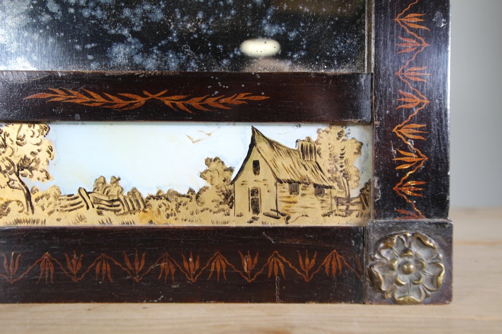 An early 19th-century rectangular wall mirror featuring a dark painted wooden frame with stencilled foliate borders and two reverse-painted glass panels displaying rural landscape scenes. View V