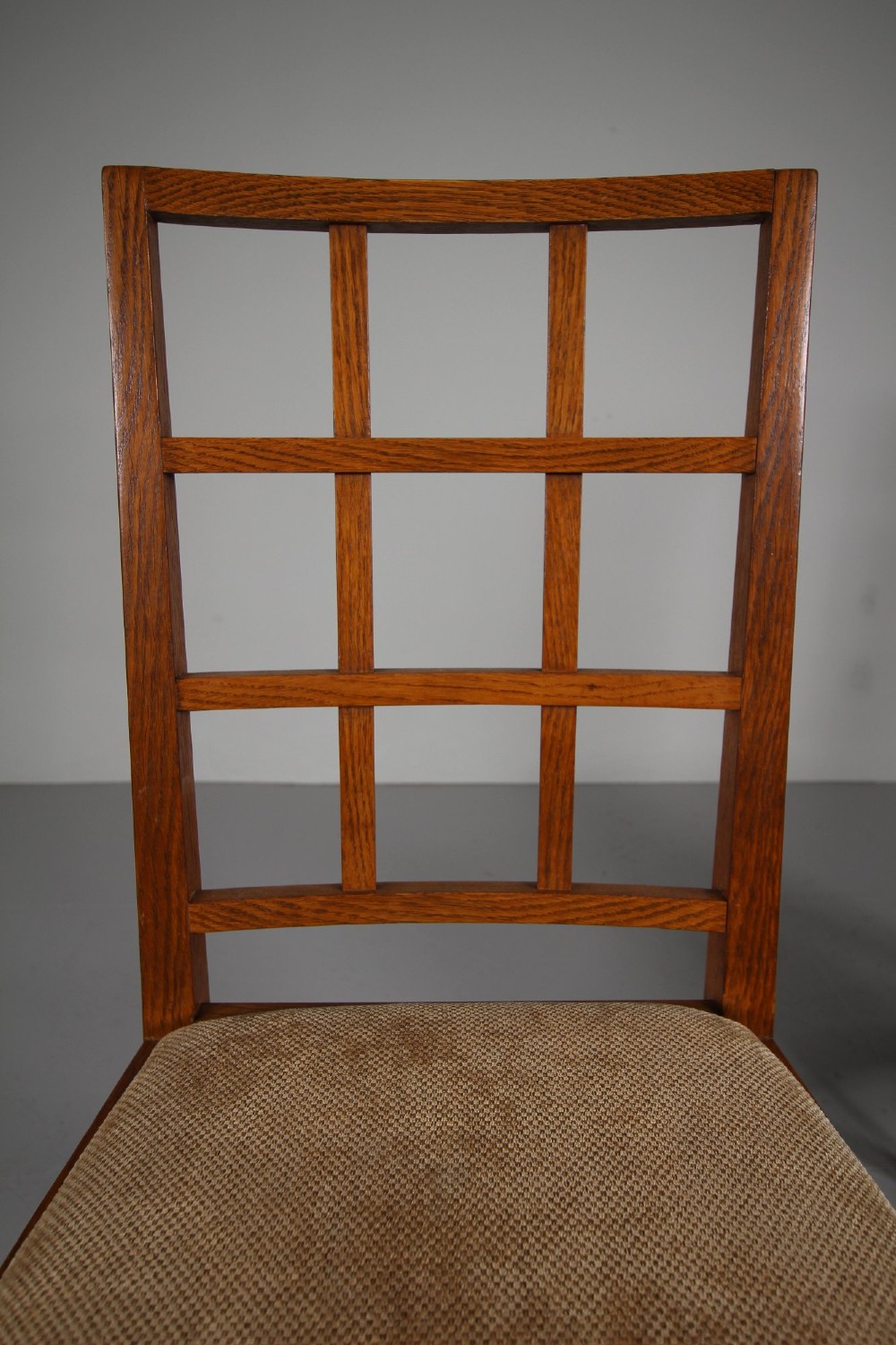 A set of six 1930s solid oak dining chairs featuring geometric lattice backs and upholstered neutral fabric seats. View V