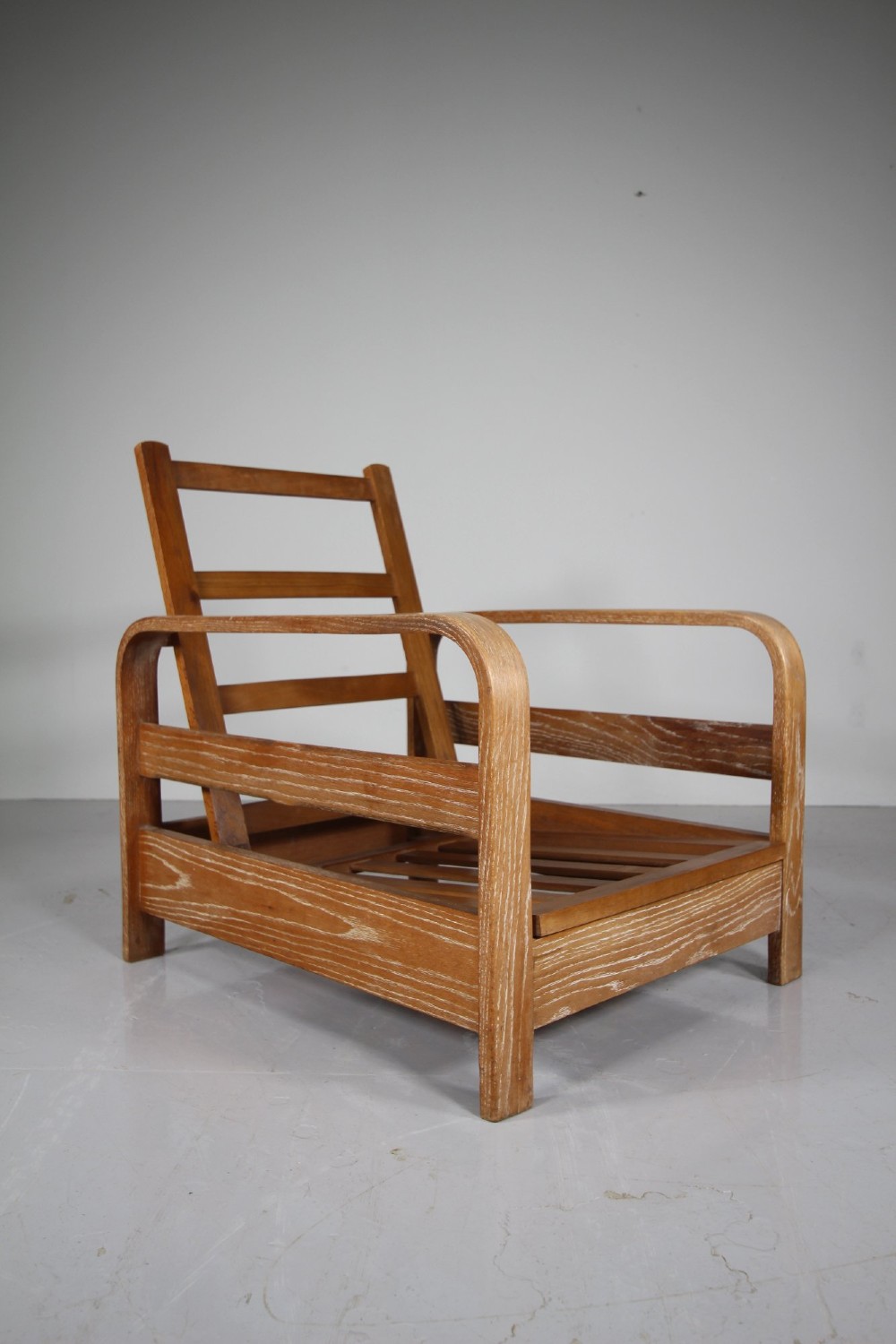 A 1930s solid oak reclining armchair frame featuring curved bentwood armrests, a slatted timber backrest, and an un-upholstered seat base.