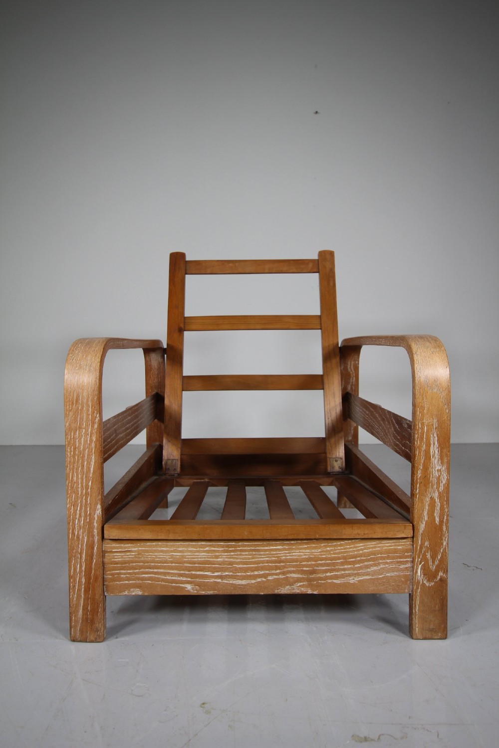 A 1930s solid oak reclining armchair frame featuring curved bentwood armrests, a slatted timber backrest, and an un-upholstered seat base. View VI