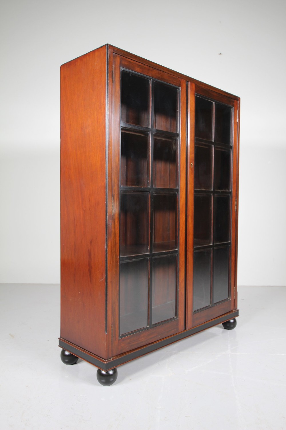 A 1920s Heals mahogany bookcase featuring two glazed doors with multi-pane glass and dark turned bun feet. View III