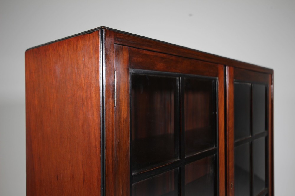 A 1920s Heals mahogany bookcase featuring two glazed doors with multi-pane glass and dark turned bun feet. View VII