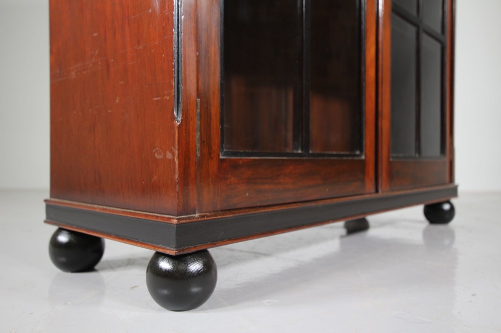A 1920s Heals mahogany bookcase featuring two glazed doors with multi-pane glass and dark turned bun feet. View VIII