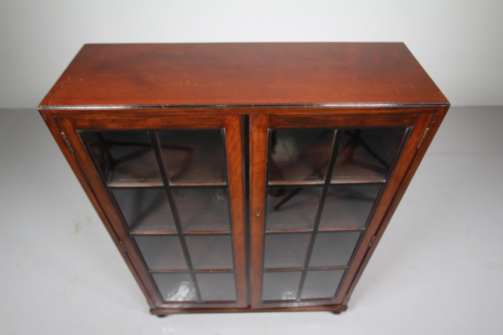 A 1920s Heals mahogany bookcase featuring two glazed doors with multi-pane glass and dark turned bun feet. View IX