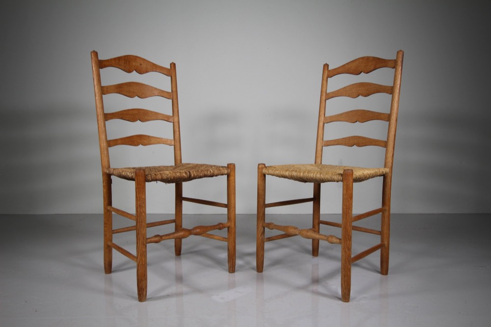 A pair of Arts and Crafts oak ladderback side chairs featuring hand-woven rush seats and four shaped back slats.