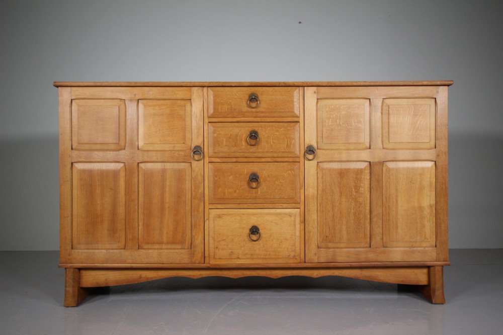 A light oak dresser base from the 1930s featuring a central stack of four drawers flanked by two panelled cupboard doors with brass ring handles.