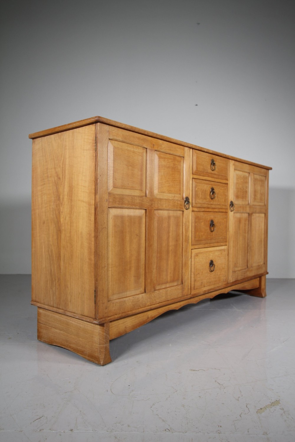 A light oak dresser base from the 1930s featuring a central stack of four drawers flanked by two panelled cupboard doors with brass ring handles. View VI