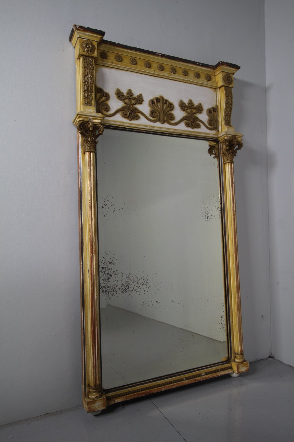 A tall nineteenth-century English Regency pier mirror featuring a cream and gilt frame flanked by fluted Corinthian columns and a decorated frieze.