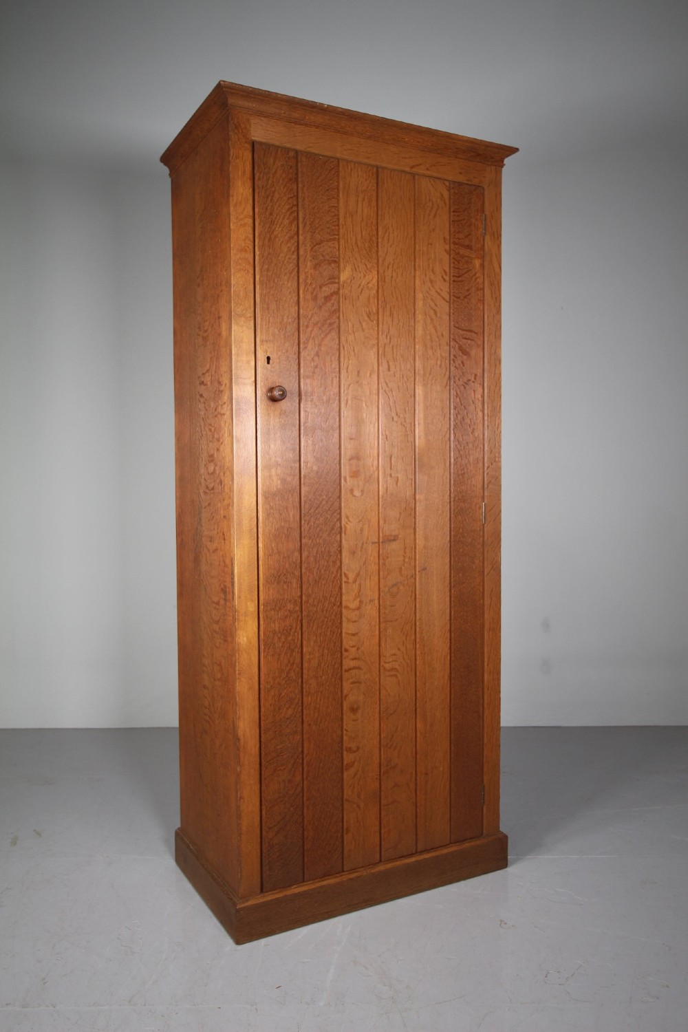 A tall single-door solid oak cupboard featuring vertical plank door construction, a wooden knob handle, and a simple plinth base. View II