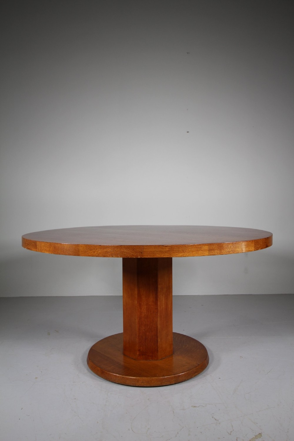 A 1930s circular oak dining table featuring a thick round top on a central octagonal pedestal column and round plinth base.