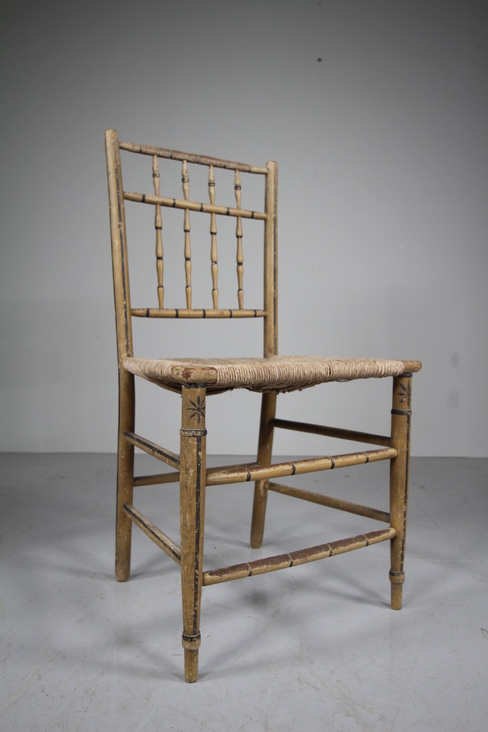 An antique English side chair featuring an ochre painted wooden frame with turned spindles, hand-painted accents, and a woven rush seat. View V