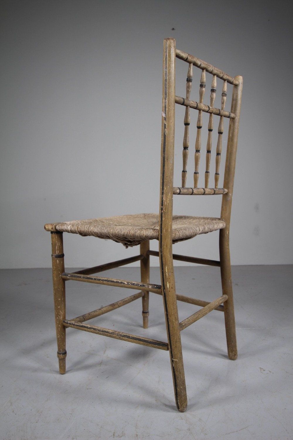 An antique English side chair featuring an ochre painted wooden frame with turned spindles, hand-painted accents, and a woven rush seat. View VI