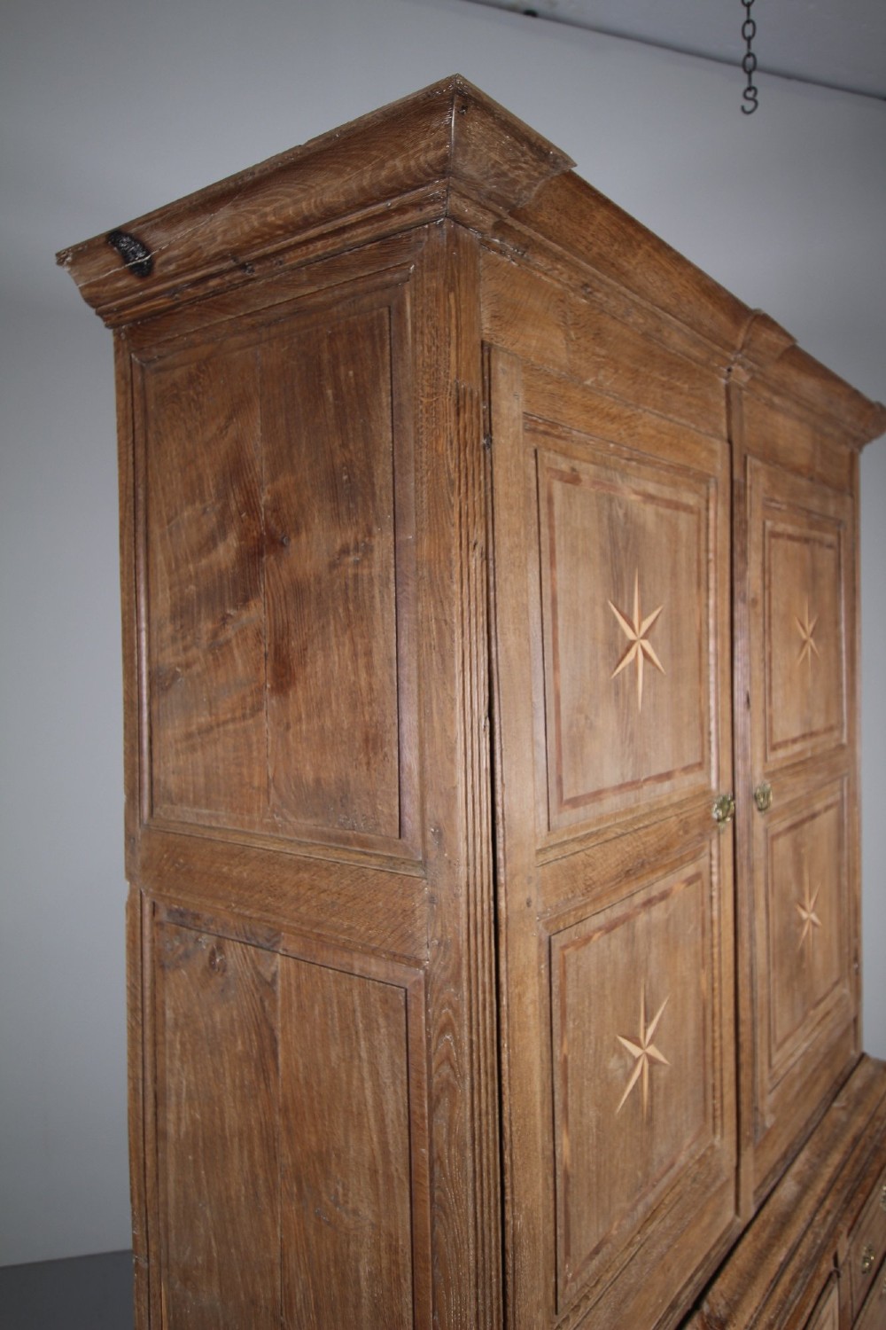 A tall two-part 17th-century Welsh oak press cupboard featuring panelled doors with star inlay motifs above a chest base with multiple drawers. View II