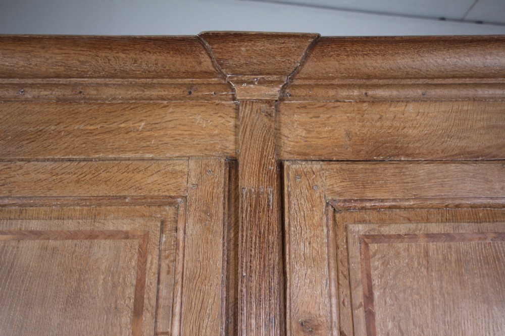 A tall two-part 17th-century Welsh oak press cupboard featuring panelled doors with star inlay motifs above a chest base with multiple drawers. View V