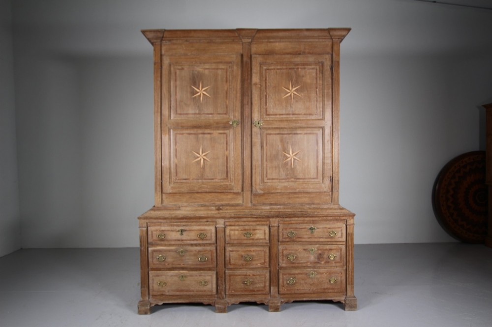 A tall two-part 17th-century Welsh oak press cupboard featuring panelled doors with star inlay motifs above a chest base with multiple drawers. View XI