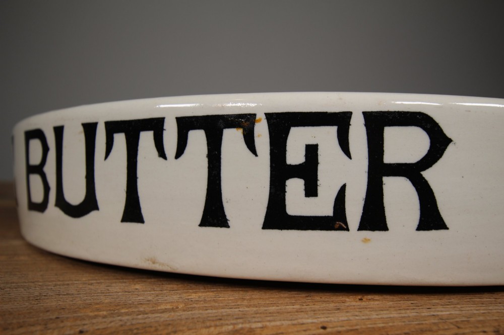 A circular creamware glazed ceramic butter slab featuring the words PURE BUTTER printed in black bold serif typography along the rim. View IV