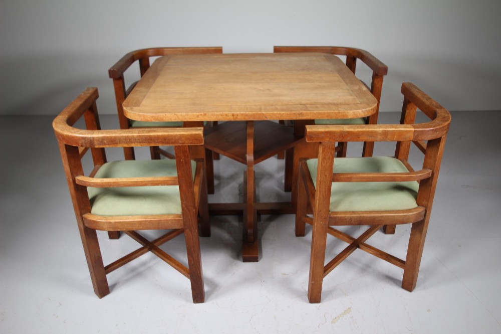 A square natural oak dining table surrounded by four matching curved-back armchairs with green upholstered seats. View VI