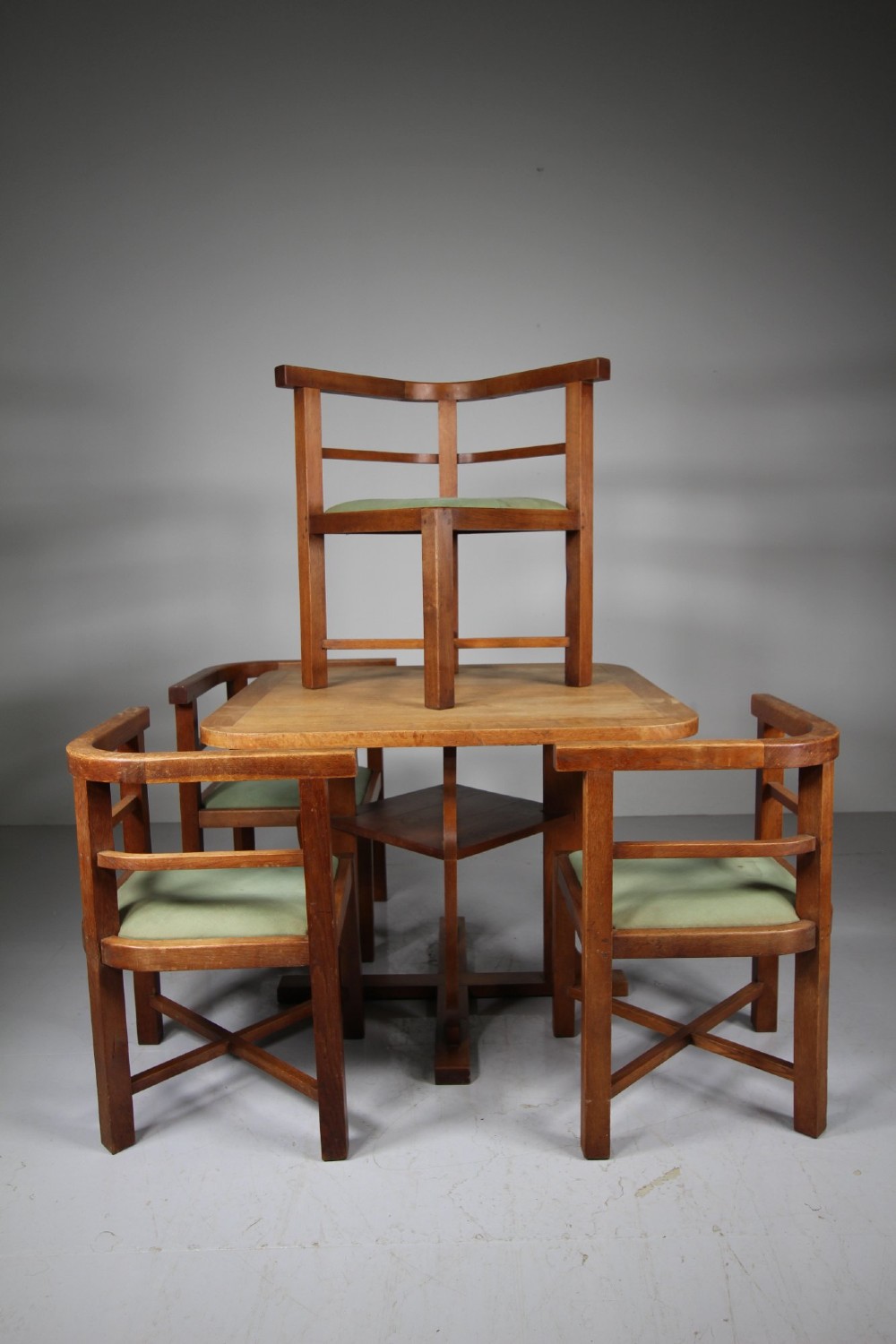 A square natural oak dining table surrounded by four matching curved-back armchairs with green upholstered seats. View VII