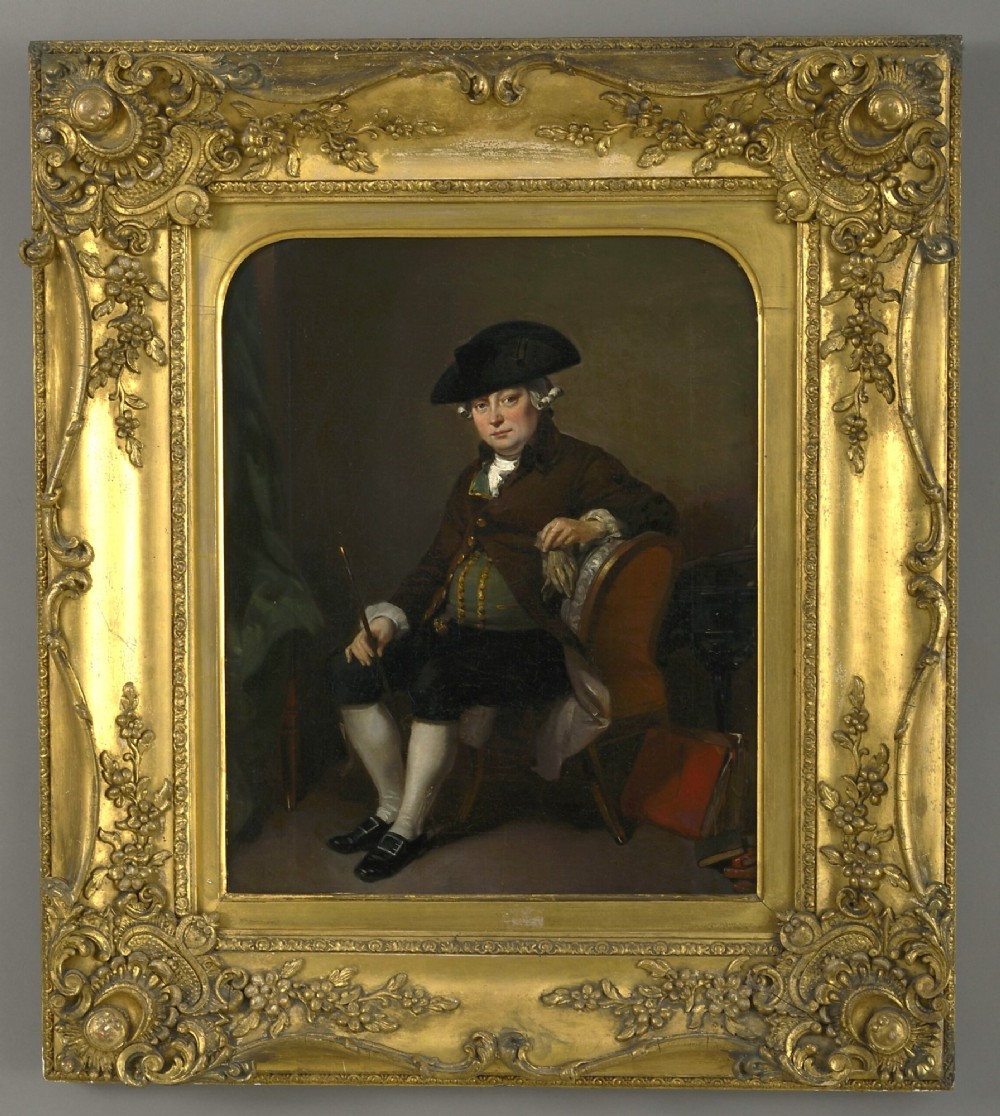 An antique oil painting depicting a seated actor in 18th-century attire holding a cane, displayed inside an elaborate gold gilt frame.