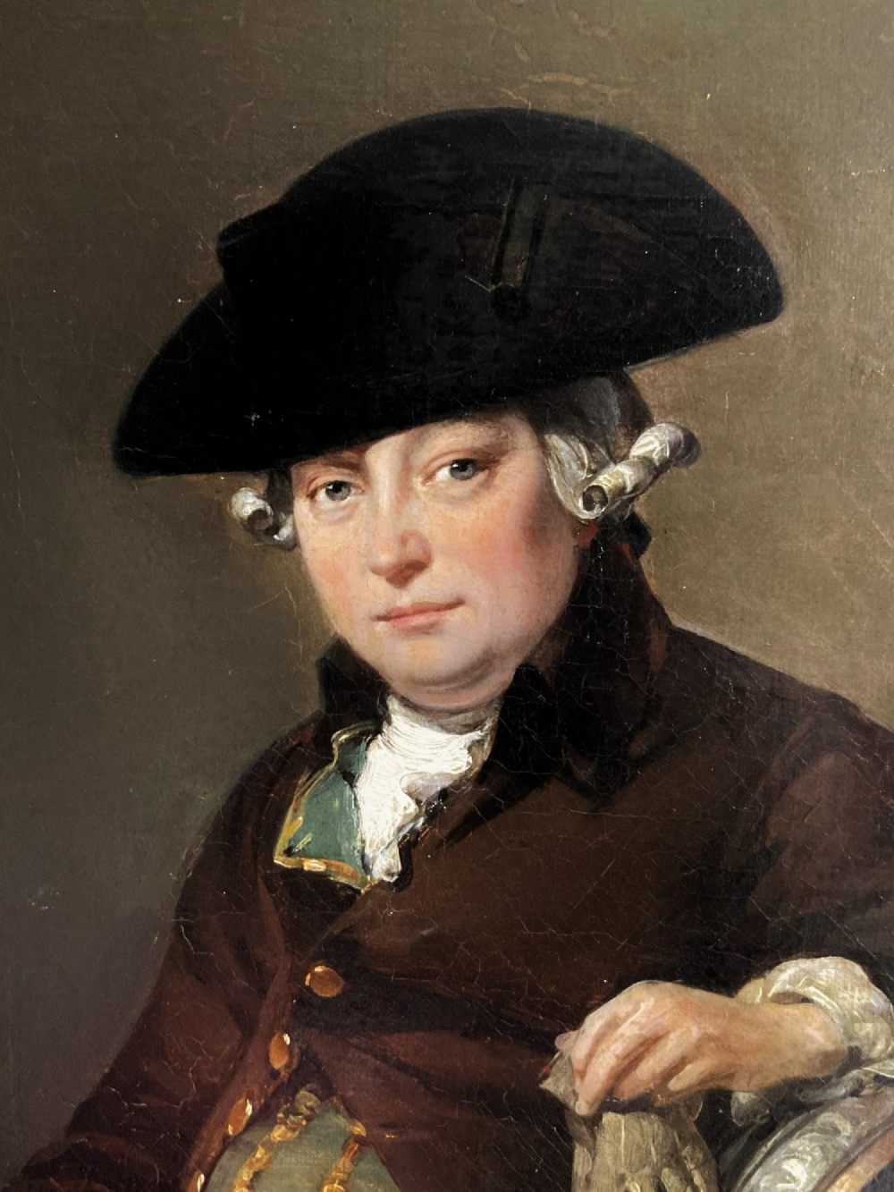 An antique oil painting depicting a seated actor in 18th-century attire holding a cane, displayed inside an elaborate gold gilt frame. View III