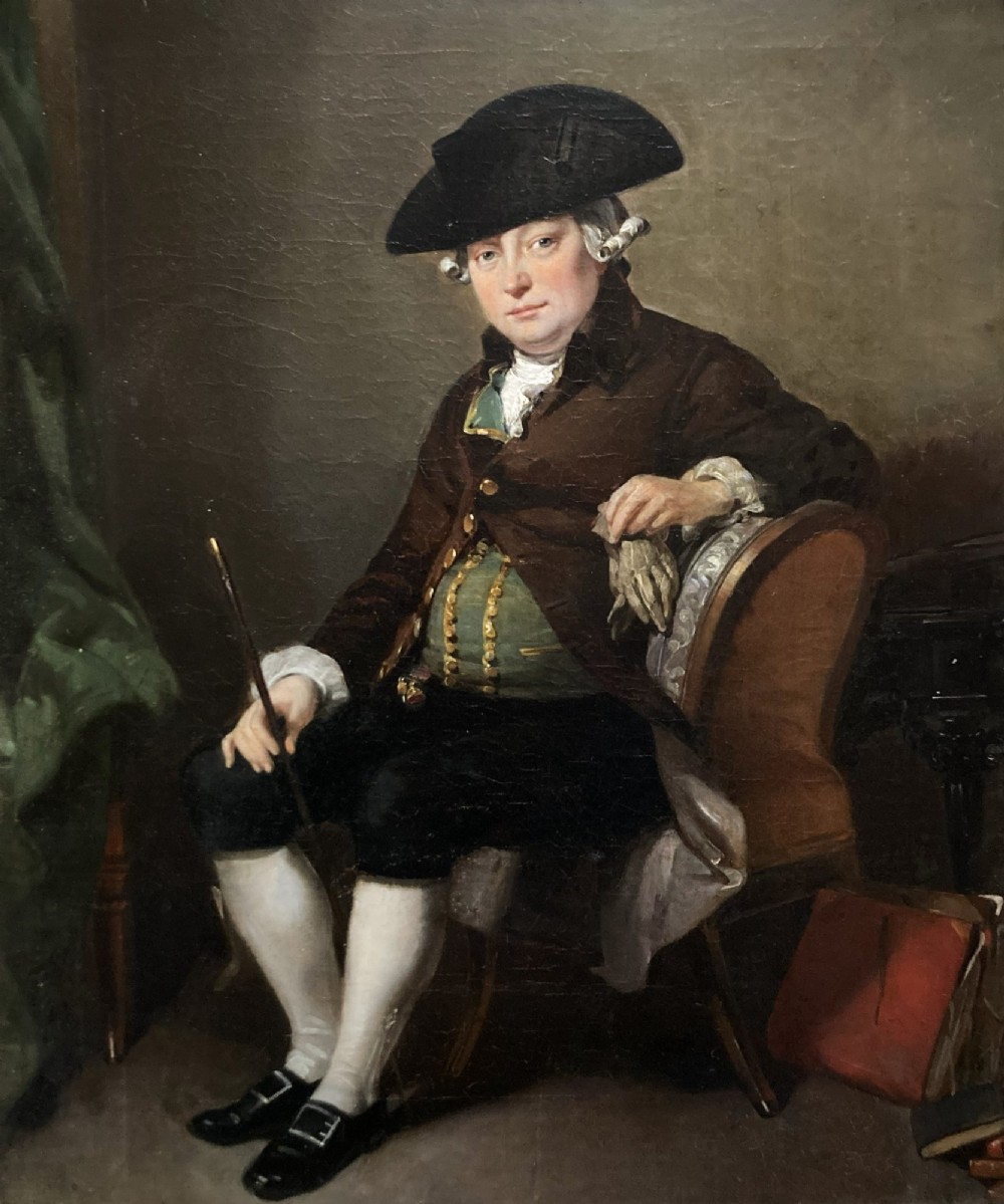 An antique oil painting depicting a seated actor in 18th-century attire holding a cane, displayed inside an elaborate gold gilt frame. View IV