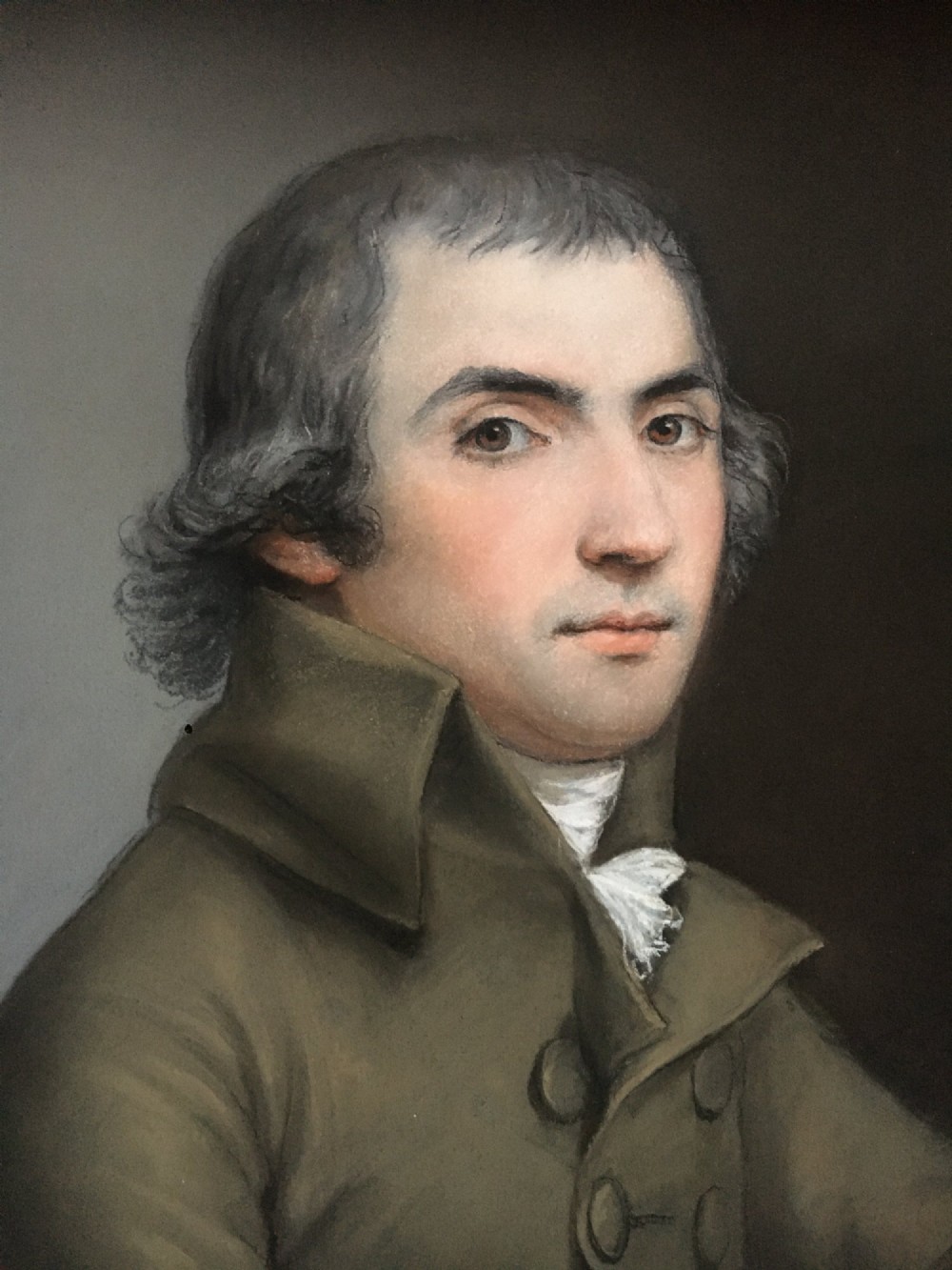 An oval portrait of a gentleman wearing a brown jacket, set within a square gilded spandrel frame and dark outer ebonised border. View II